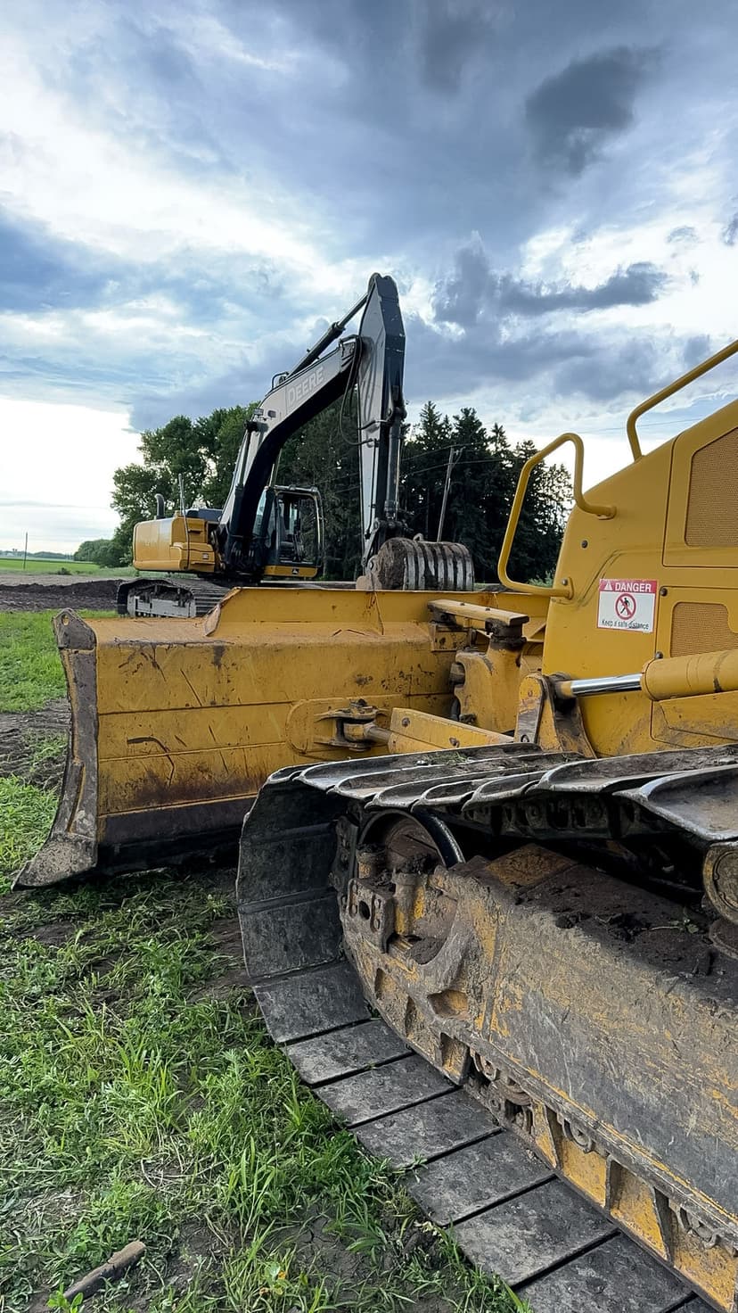 Excavator and bulldozer working on construction site under cloudy sky.
