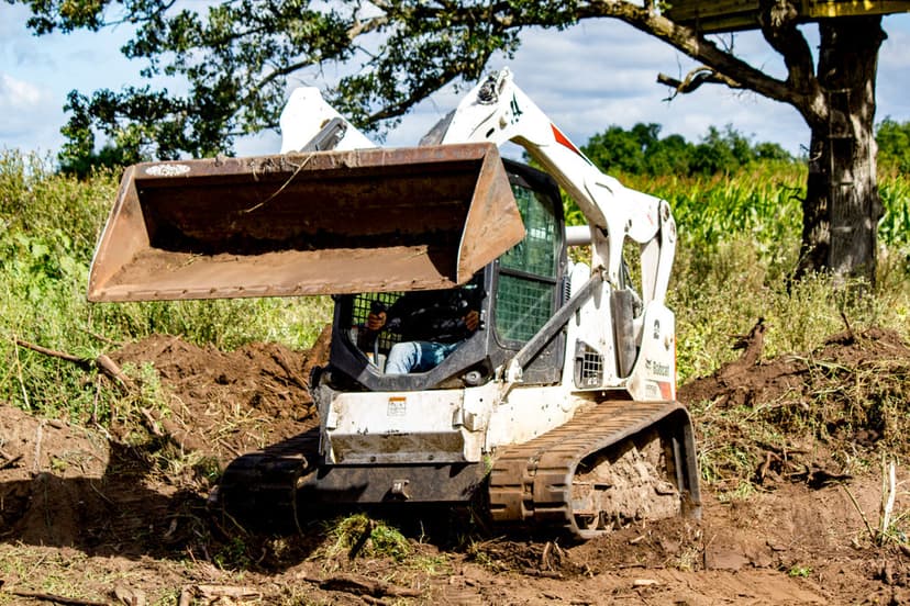 Bobcat skid steer loader clearing debris in a field under a blue sky.