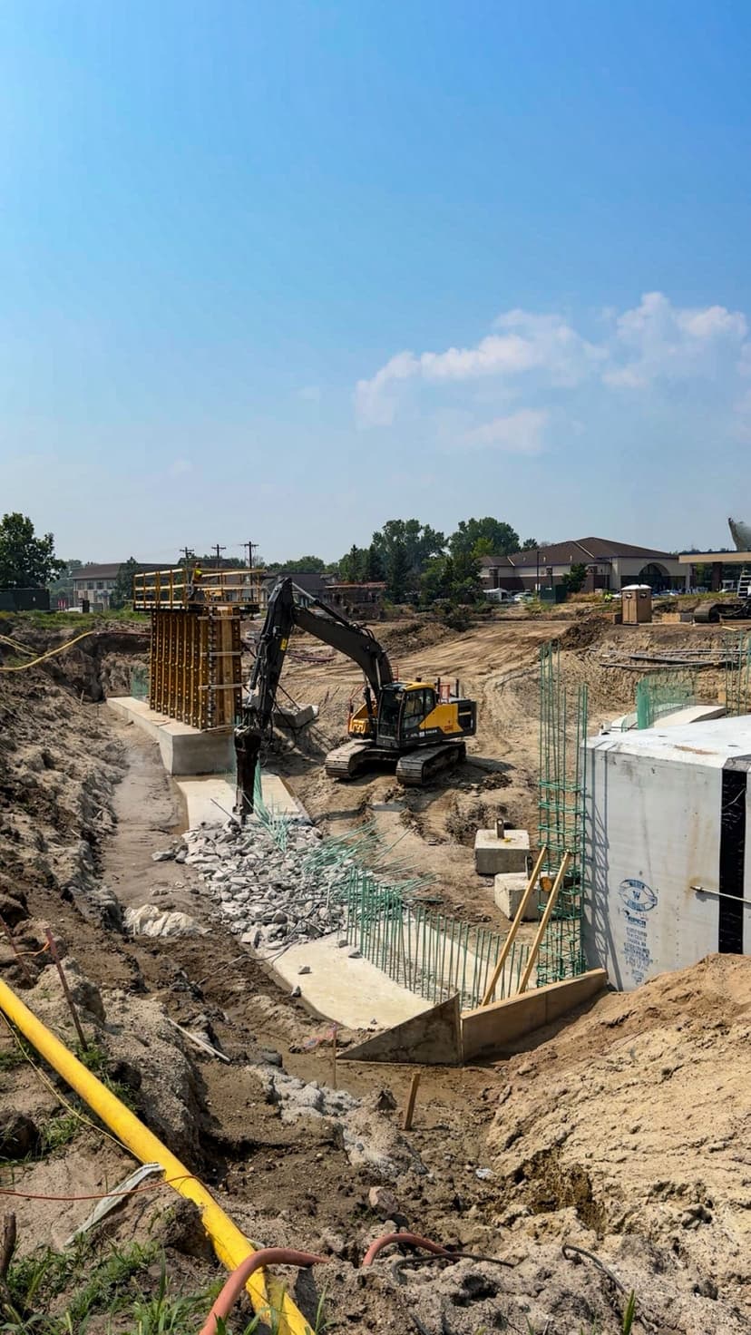 Excavation site with machinery working on foundation and concrete structures under blue sky.