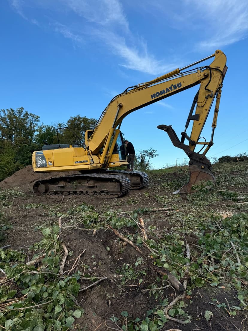 Komatsu excavator working on land clearing with debris and blue sky in the background.