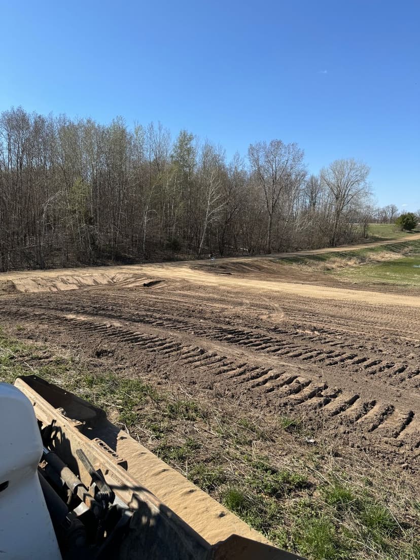 Cleared landscape with tire tracks, surrounded by trees and blue sky. Ideal for construction projects.