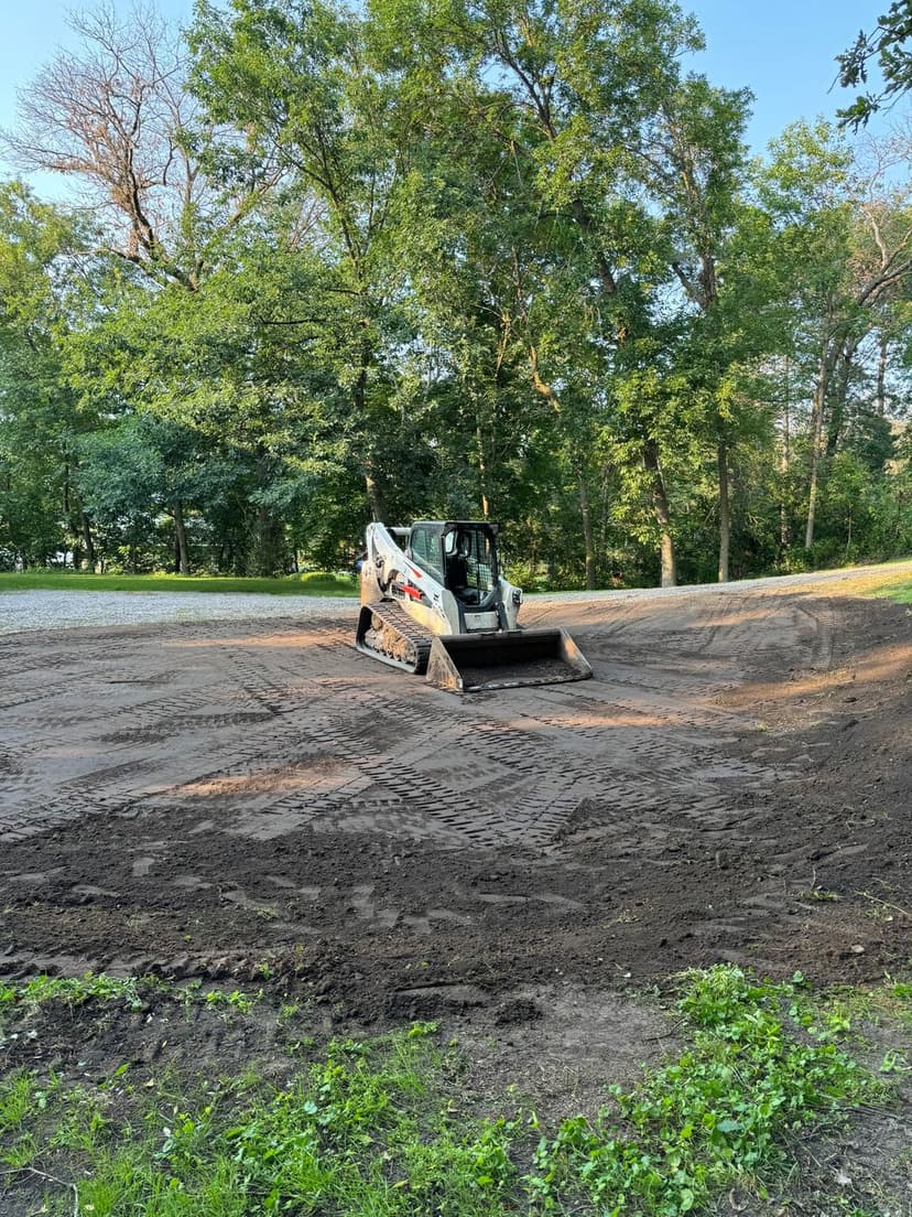 Bobcat skid steer loader leveling a dirt surface in a wooded area.